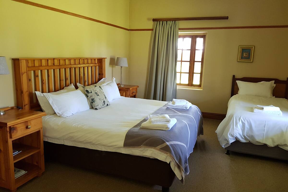 A hotel room with a large bed, two bedside tables, a nightstand, a window with curtains, and a framed picture on the wall.