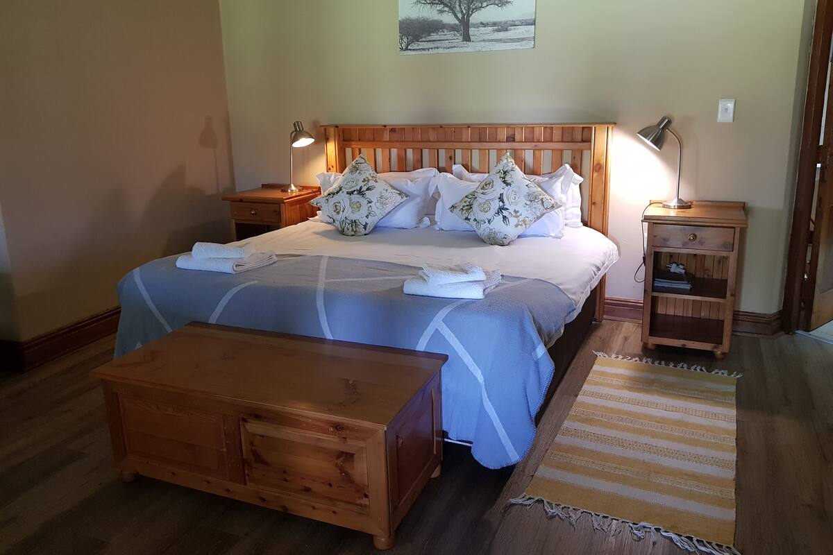 A neatly arranged bedroom with a wooden bed, bedside tables with lamps, a wooden bench, and a rug.