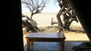 A wooden table in a room with a view of a desert landscape and a large tree. - Francolin Creek (Ngwathe)