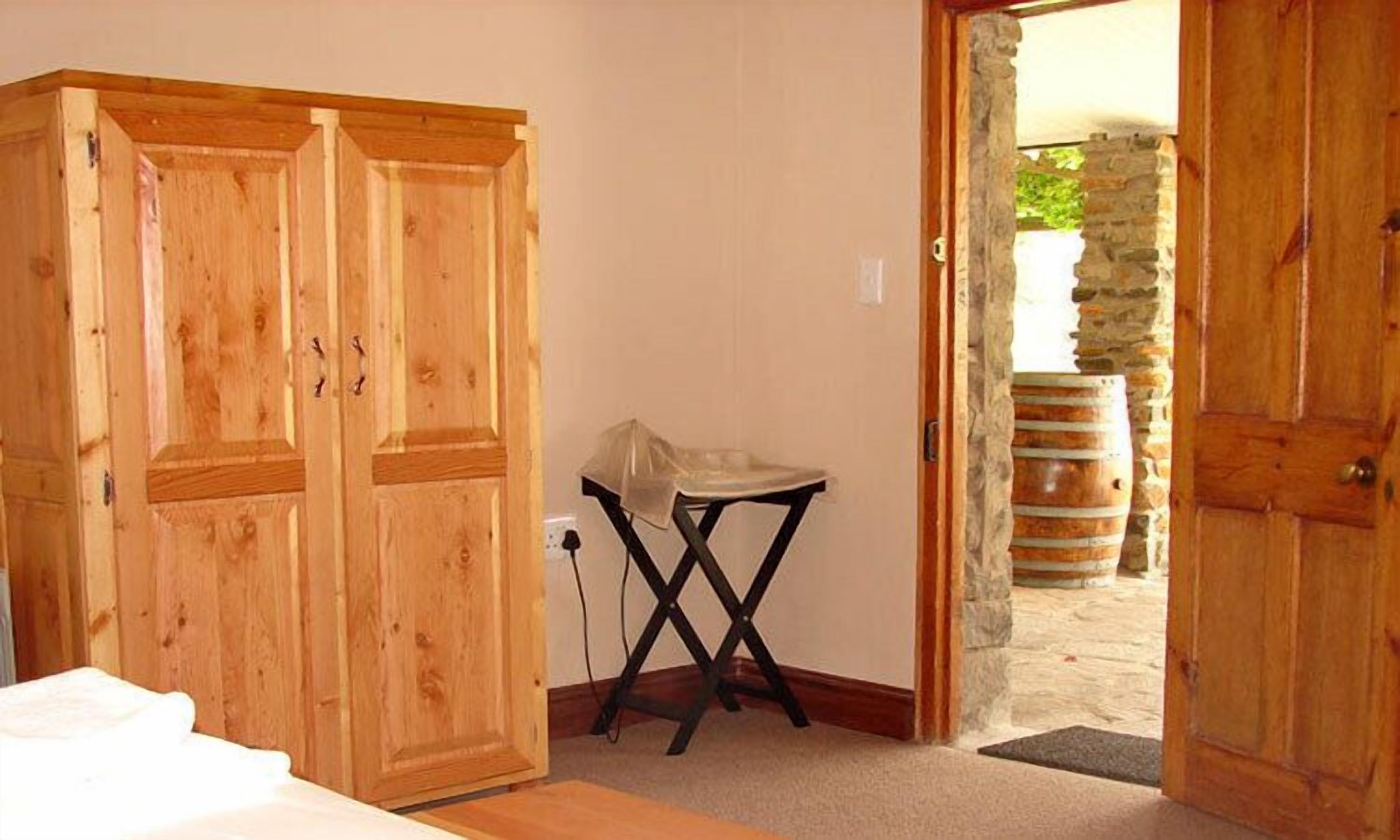 Una habitación con puertas dobles de madera, una pequeña mesa cubierta con un mantel y una pared de piedra visible a través de un acceso abierto.