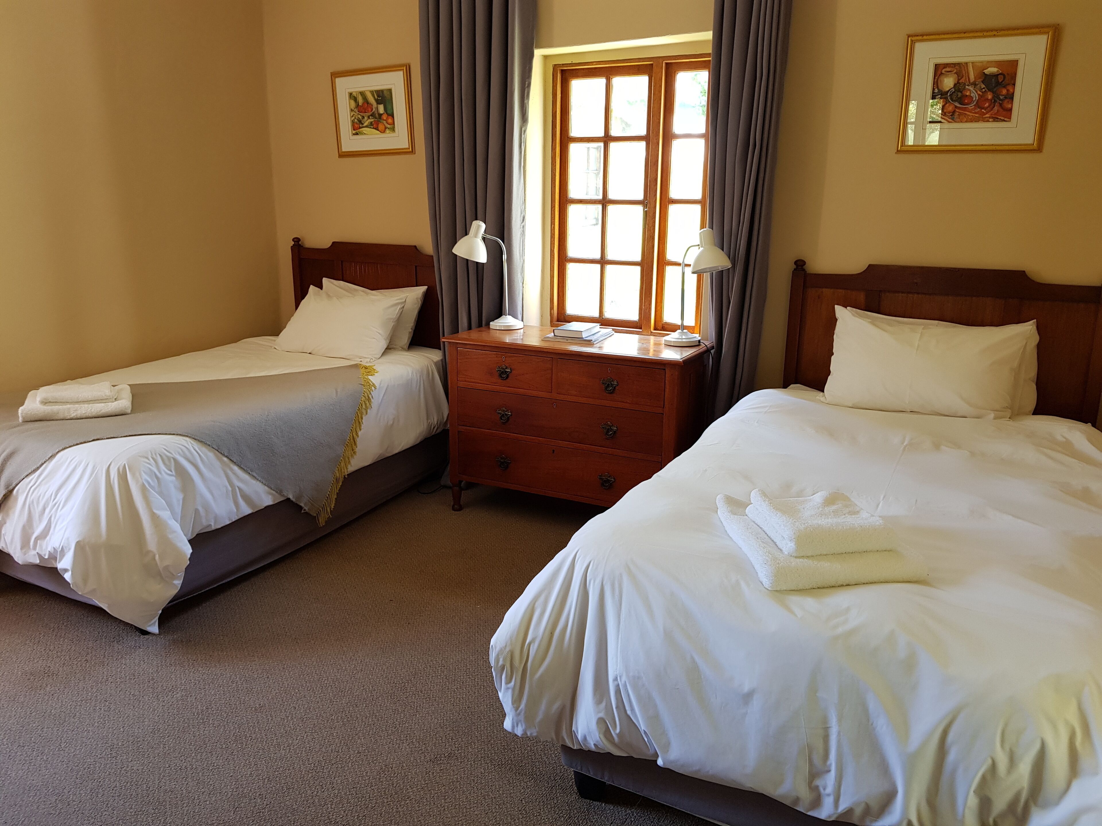 A hotel room with two beds, a wooden dresser, and a window with curtains.