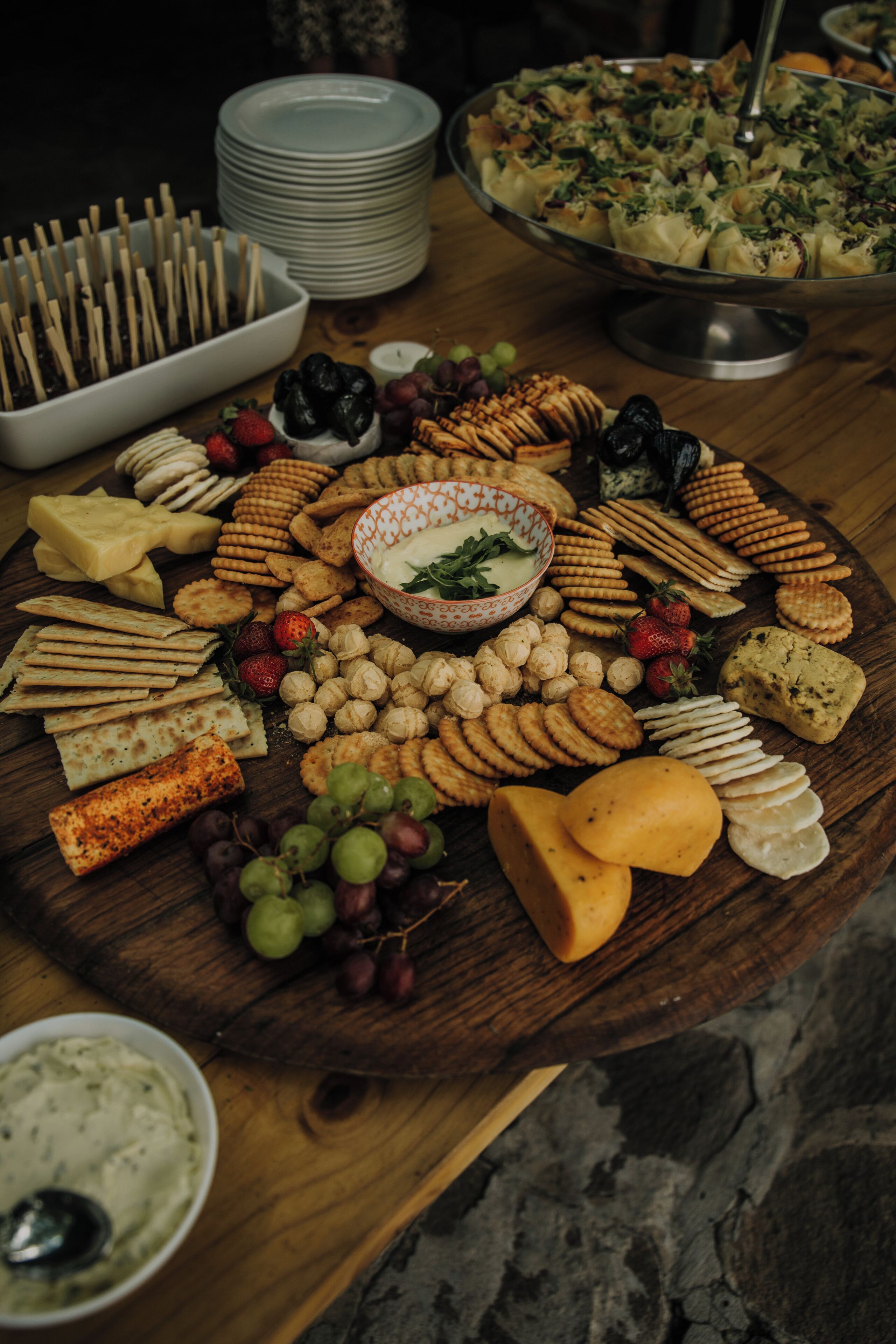 Een houten tafel met diverse kazen, crackers en fruit.