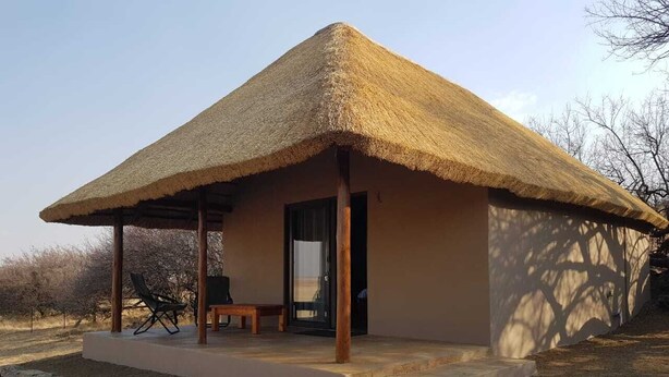 A thatched-roof structure with a covered porch, a bench, and a door. - Francolin Creek (Ngwathe)