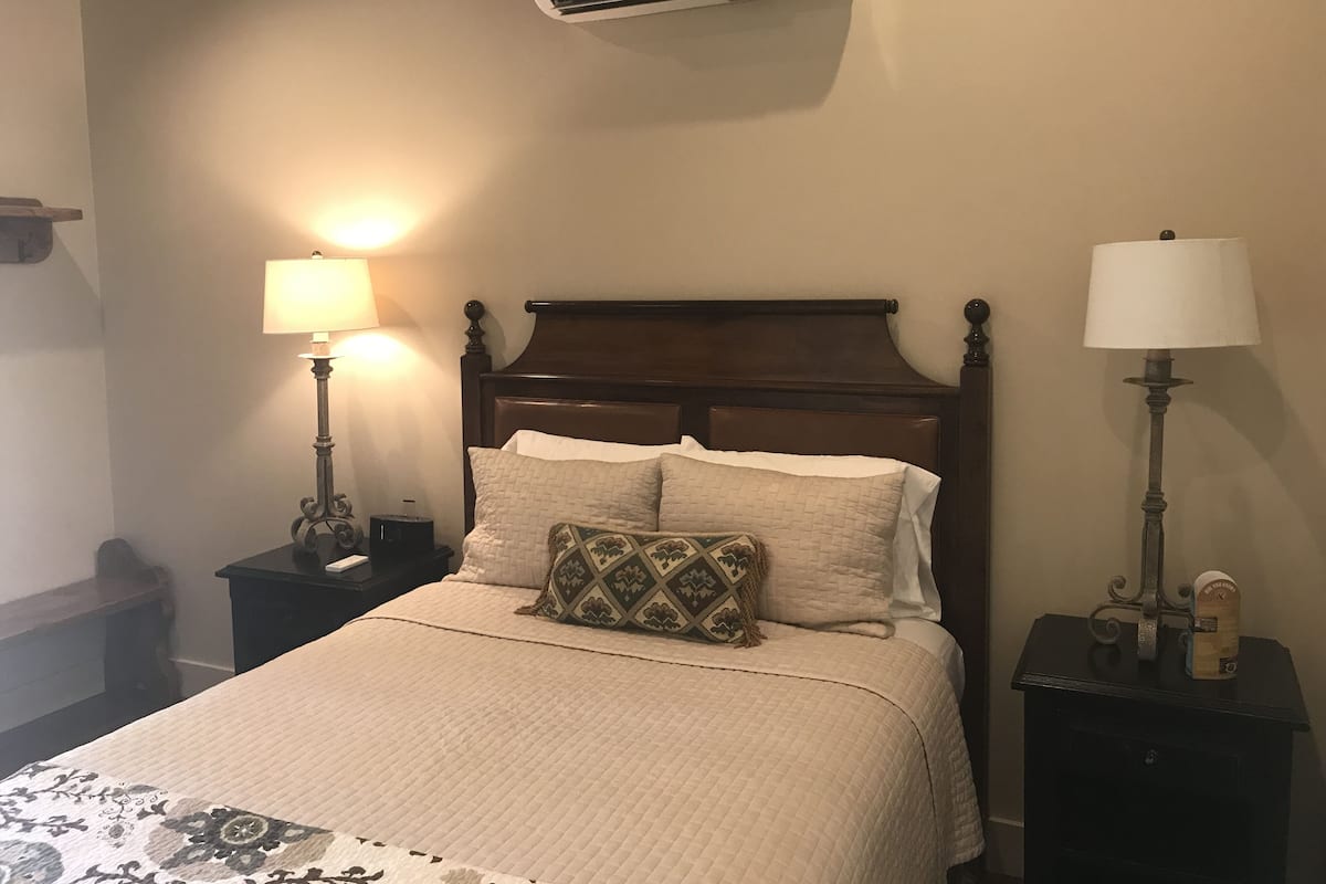 A neatly made bed with a wooden headboard, two bedside tables with lamps, and an air conditioning unit above.