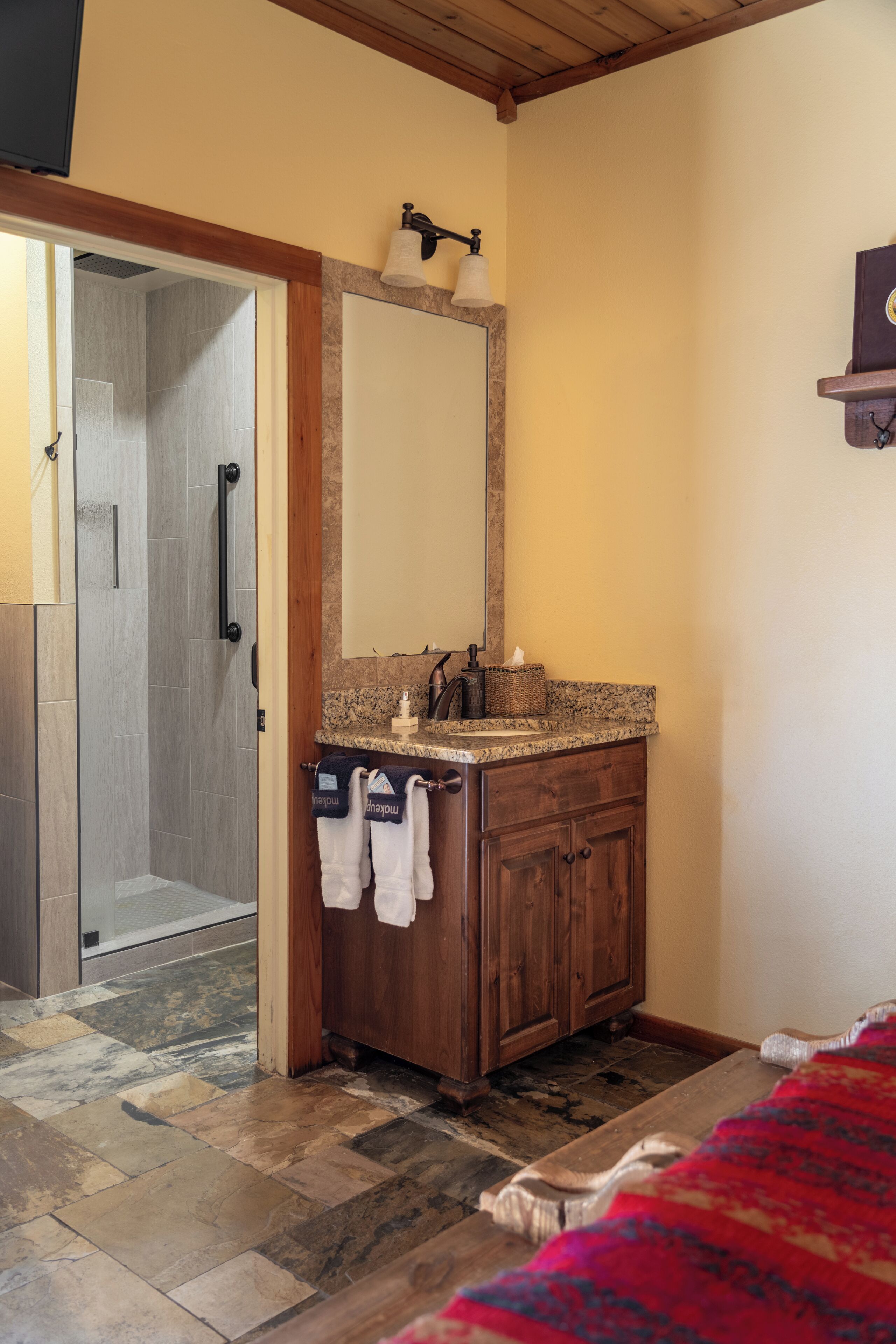 Baño con ducha, tocador de madera y un espejo grande.