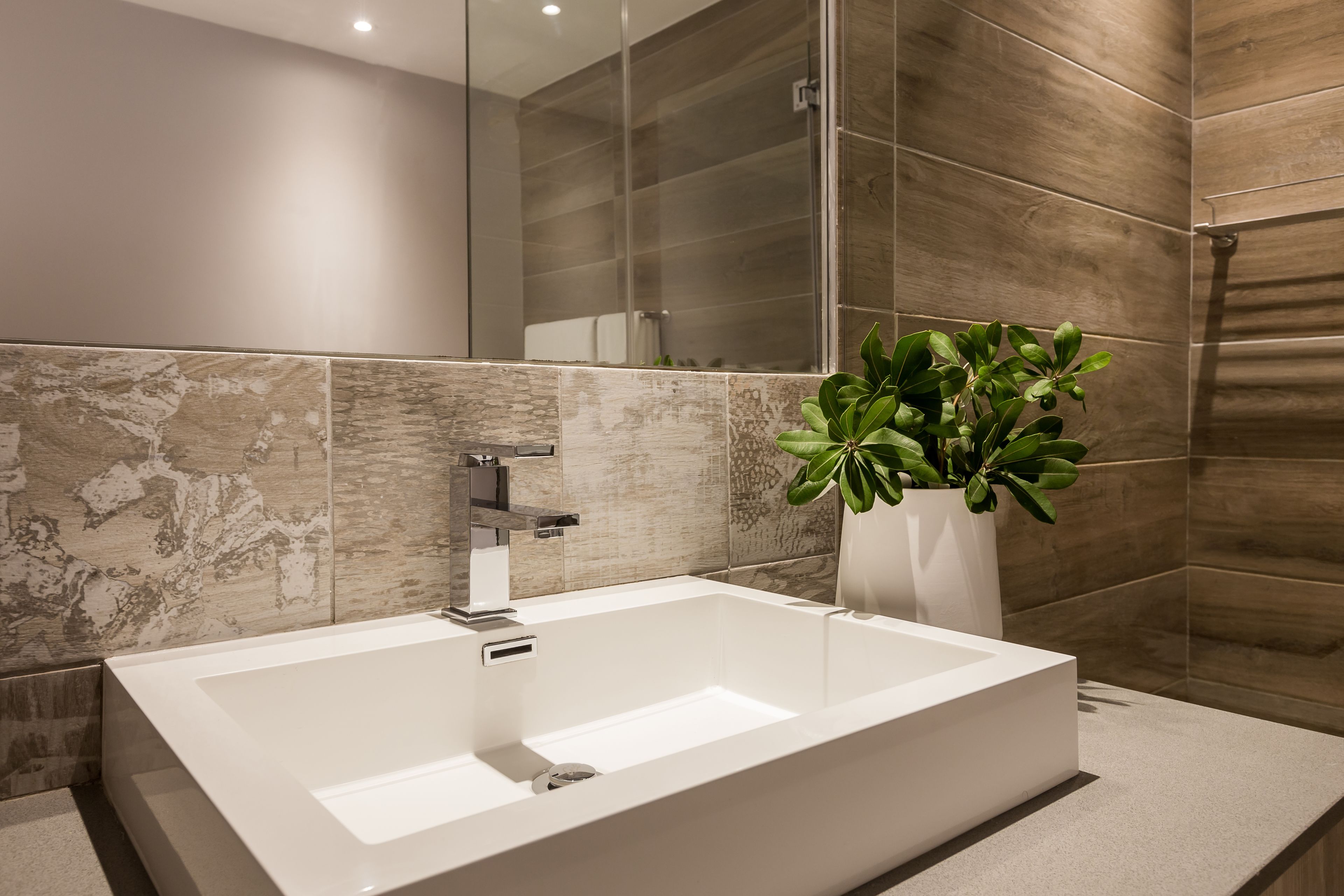 A modern bathroom with a large rectangular sink, a mirror, and a potted plant.
