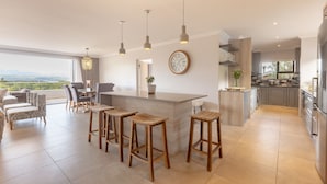 A modern kitchen with a central island, bar stools, pendant lighting, and a view of the outdoors. - Sunrise Bay Self-Catering Accommodation (Plettenberg Bay)