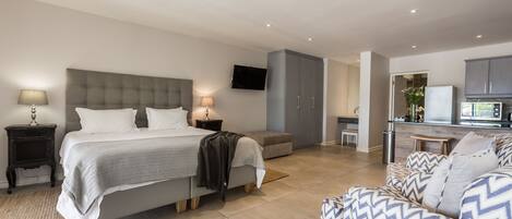 A modern bedroom with a large bed, bedside tables, a TV, and a kitchenette area.