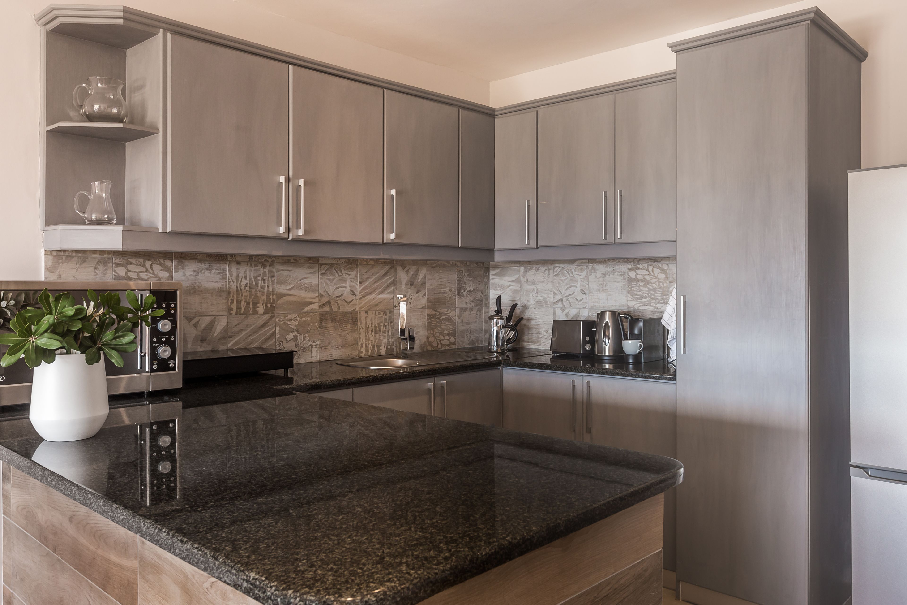 Une cuisine moderne dotée de plans de travail en granit, d’appareils électroménagers en acier inoxydable et de meubles de couleur grise.