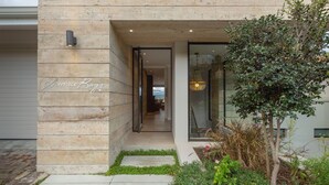A modern house with a wooden exterior, a visible name plaque, and a garden area with plants and a tree. - Sunrise Bay Self-Catering Accommodation (Plettenberg Bay)