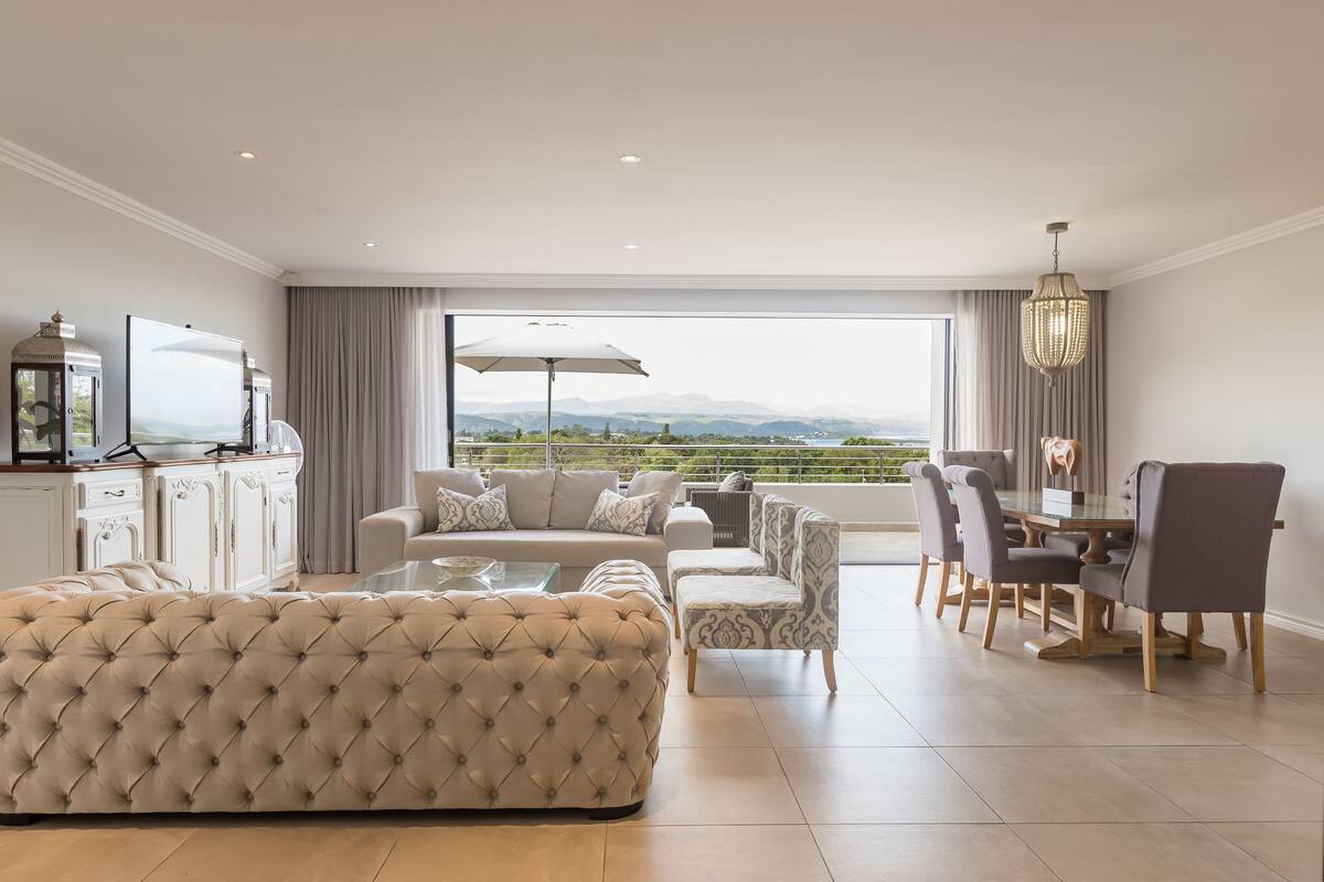 Amplia sala de estar con un ventanal grande, comedor con mesa y sillas, y zona de estar con sofá y sillones.
