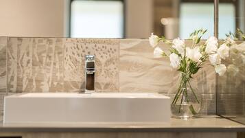 A bathroom with a marble sink, a modern faucet, and a vase with white flowers.