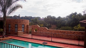 A swimming pool with a brick wall and metal railing, surrounded by trees and a clear sky.