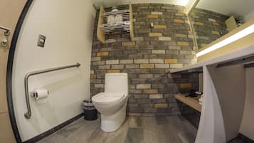 Baño compacto con inodoro, barra de apoyo, cesto de basura y repisa con artículos de aseo.