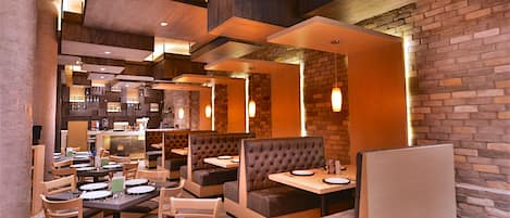 A modern restaurant interior with booths and tables, brick walls, and recessed lighting.