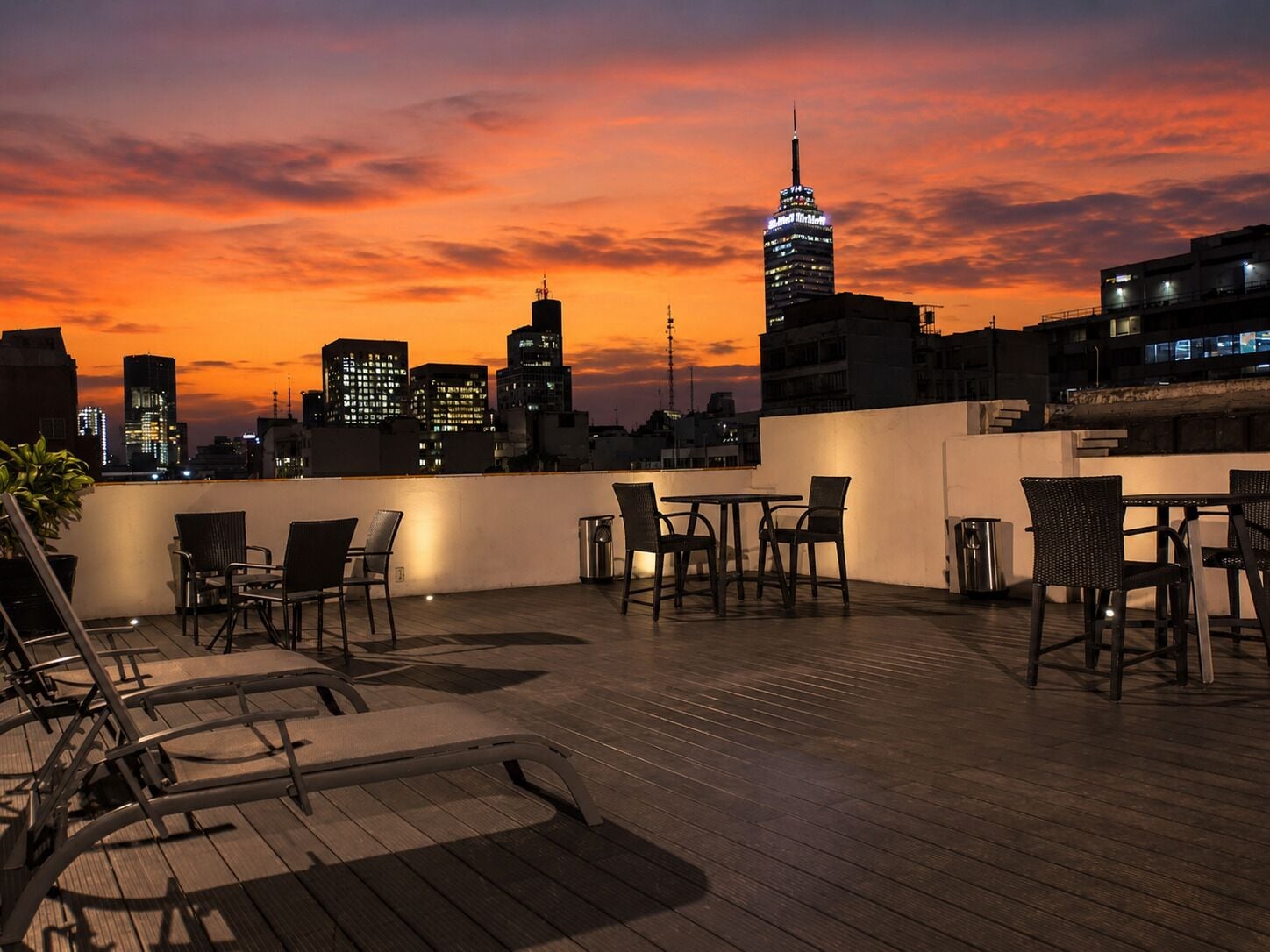 A rooftop terrace with outdoor seating, a view of the city skyline, and a sunset.