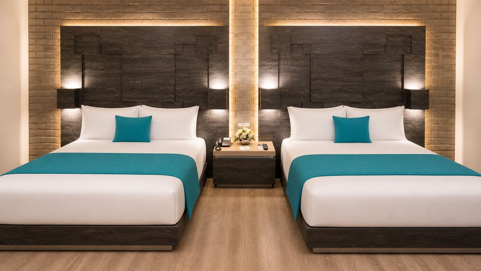 A hotel room with two beds, dark wood headboards, teal bedding, a nightstand with a phone and flowers, and a wooden floor.