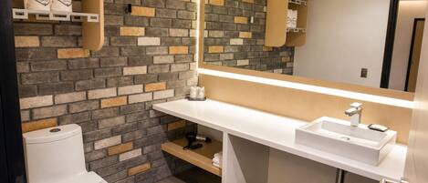 A modern bathroom with a white toilet, a white sink, and a mirror above the sink. The wall features a brick pattern.