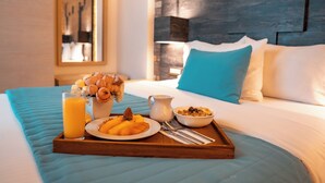 Een ontbijfwagen op een bed met een blauwe deken, een glas sinaasappelsap, een schaal fruit, een kom ontbijtgranen en een karaf melk.