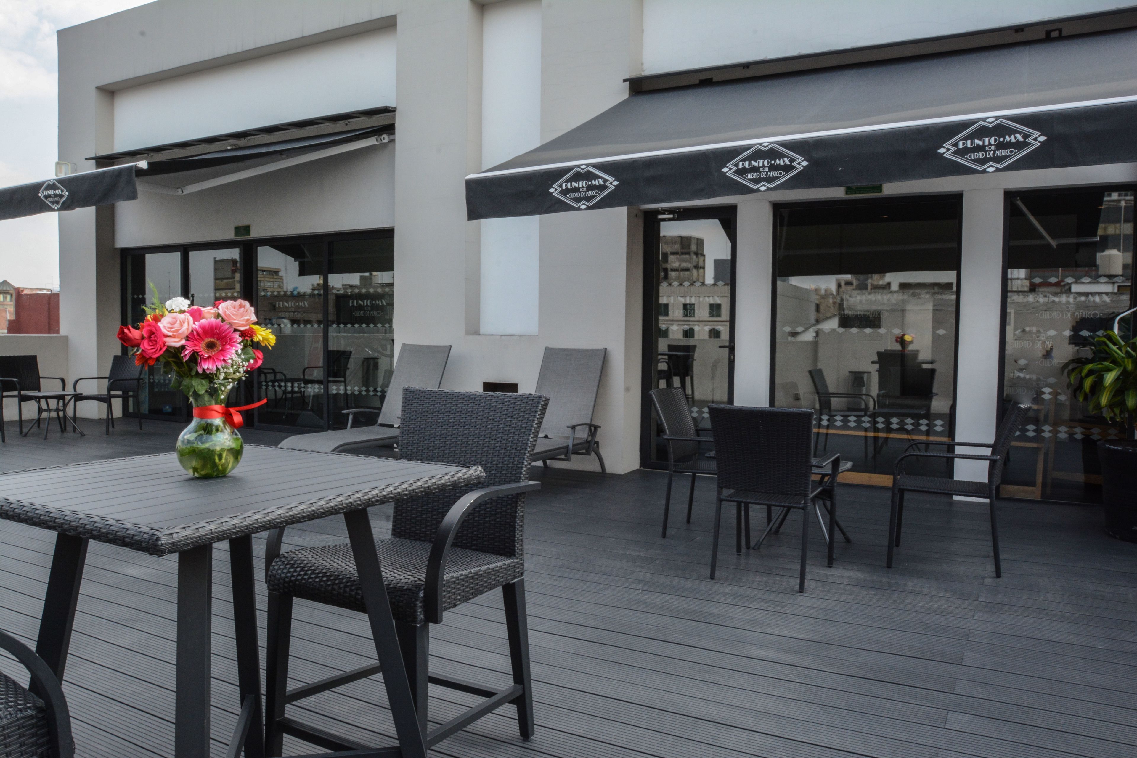 An outdoor seating area with tables and chairs, a vase of flowers, and awnings with the name "PUNTO-MX".