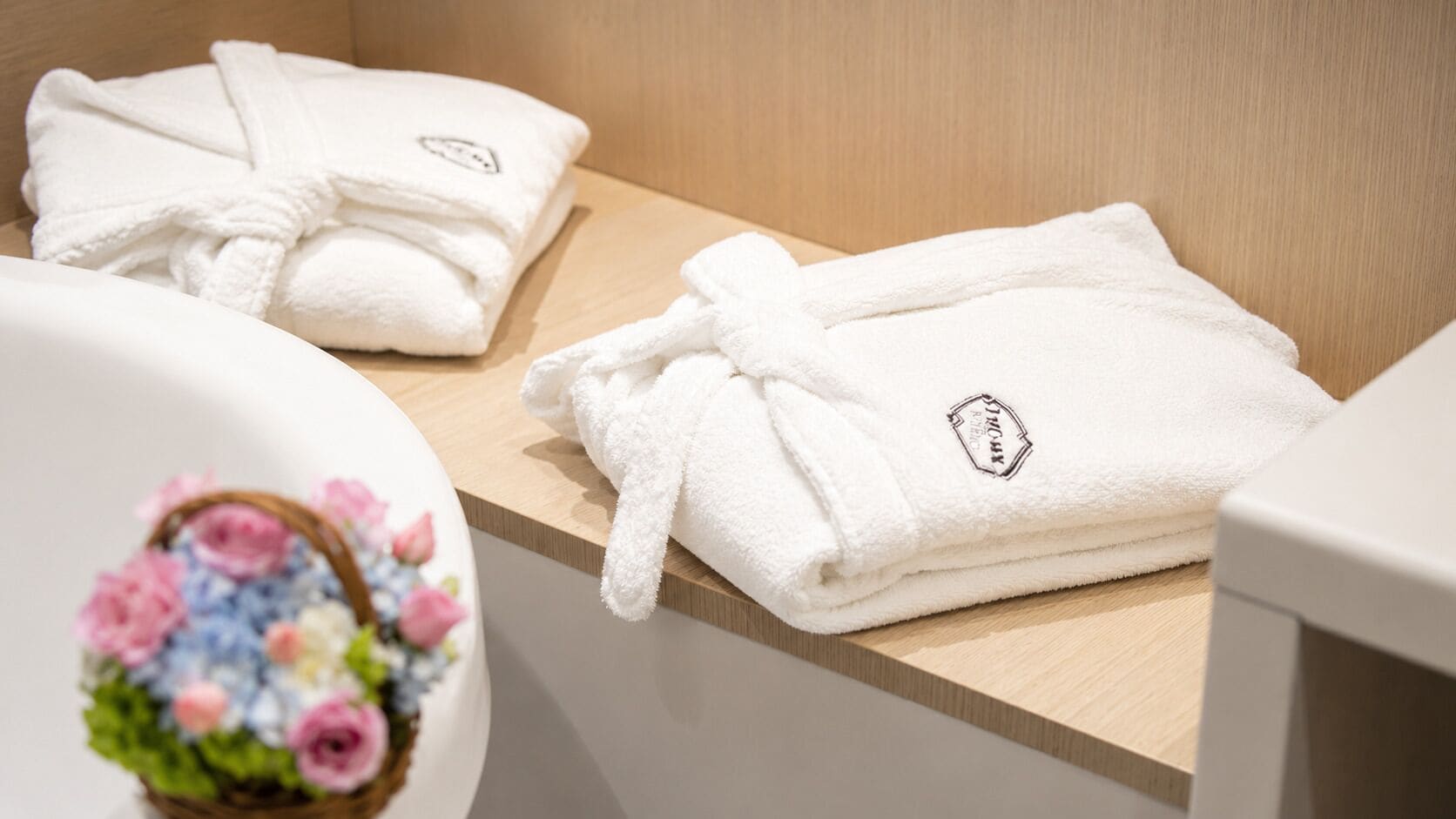 A bathroom with white towels, a wooden counter, and a small basket with flowers.