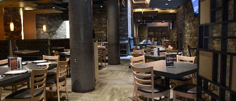 A restaurant interior with wooden tables and chairs, stone walls, and a herringbone floor pattern.