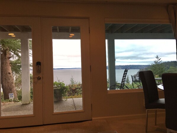 A room with a view of a lake and mountains. There is a door with glass panels, a table with chairs, and a sign indicating a smoking area.