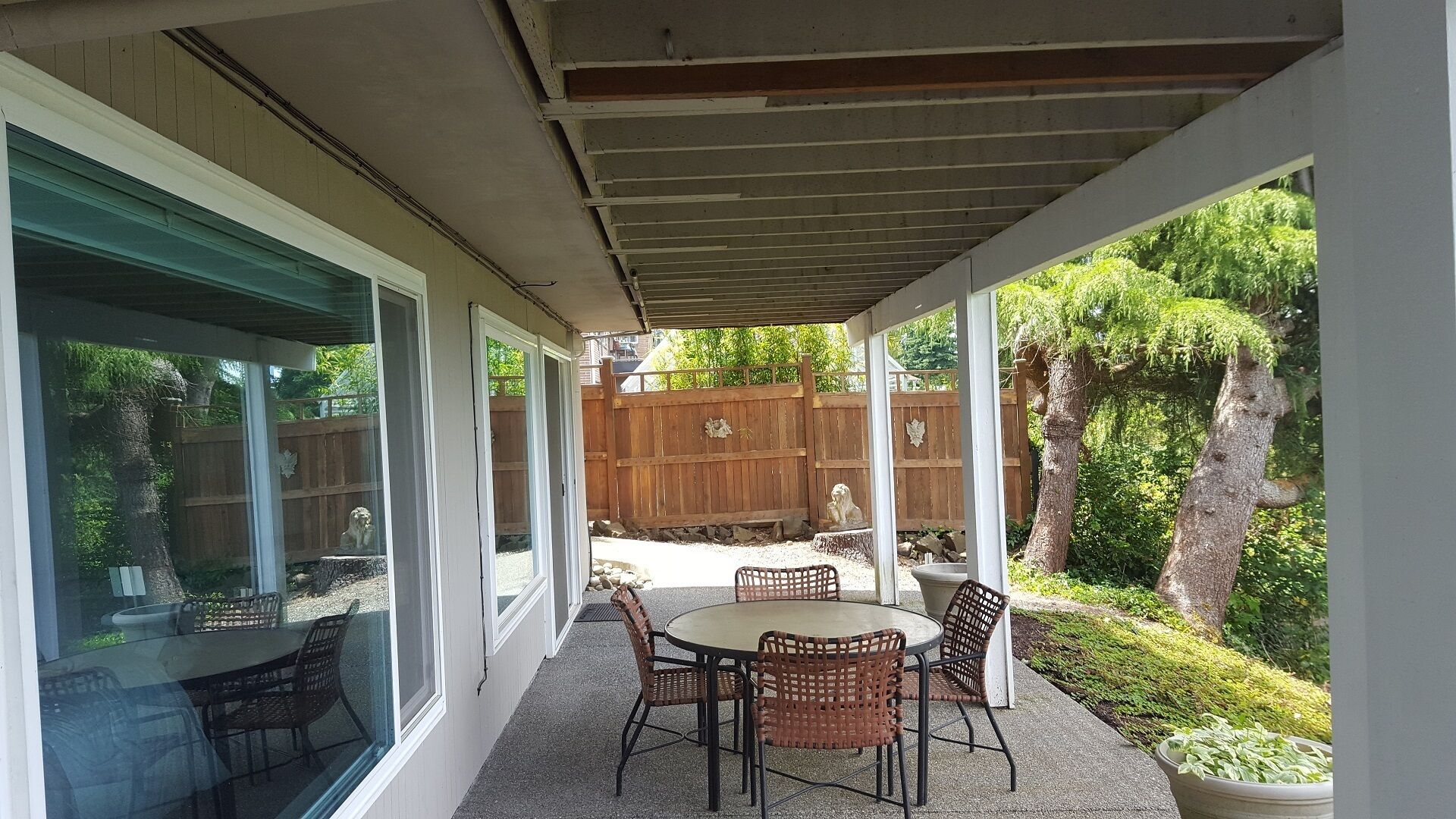 A covered patio with a round table and chairs, a wooden fence, and a tree.