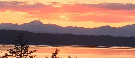 A sunset over a lake with mountains in the background and trees in the foreground.
