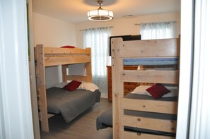 A room with two bunk beds, a wooden floor, a ceiling light fixture, and a window with curtains.