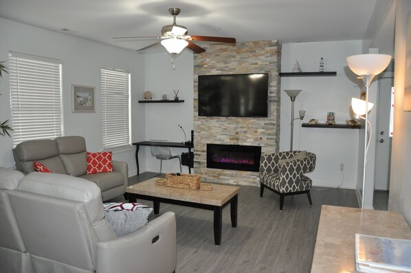 A living room with a fireplace, a television, and a ceiling fan.