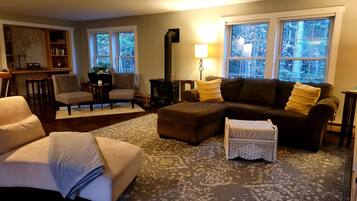 A cozy living room with a sectional sofa, armchairs, a small ottoman, and a patterned rug.