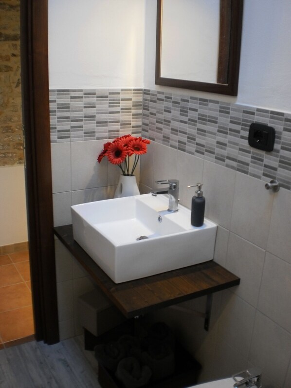 Une salle de bain avec un lavabo blanc, un miroir et un mur recouvert de carreaux.