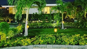 A well-lit residential area with a house, palm trees, and a well-maintained garden at night.