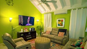 A living room with a green wall, a ceiling fan, a flat-screen TV, a sofa, a loveseat, and a patterned rug.