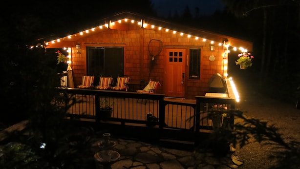 Una cabaña de madera con porche, luces colgantes y mobiliario exterior.