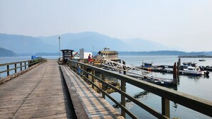 Un muelle de madera que lleva a un muelle con barcos, un camión y un pequeño edificio.