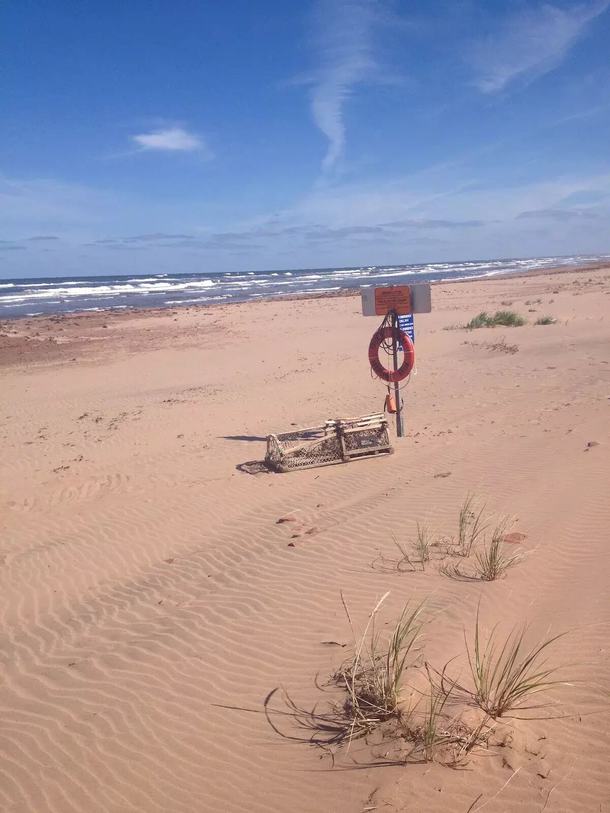 Une plage de sable avec une bouée de sauvetage et un panneau d’information.