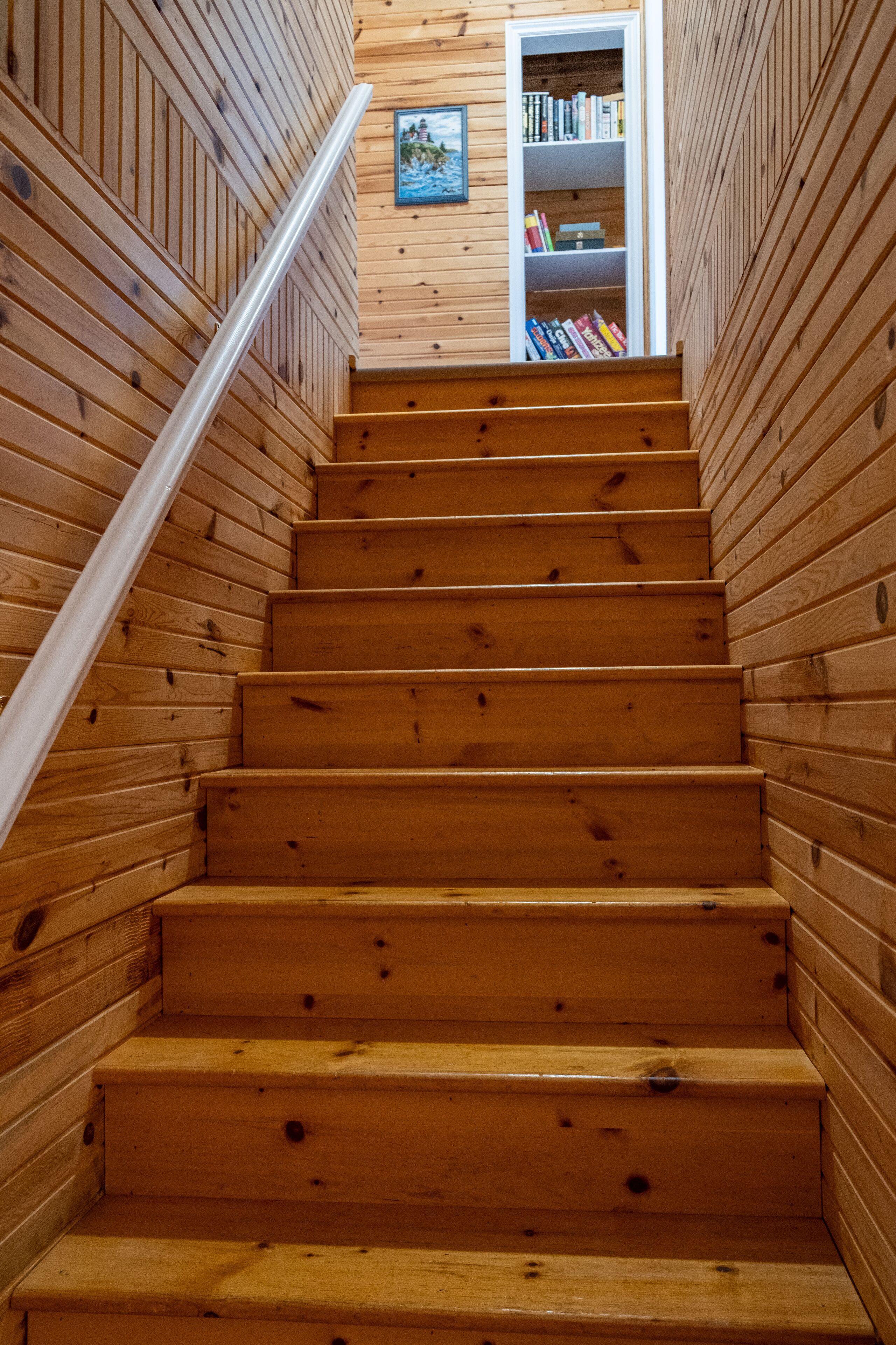 A wooden staircase with a white handrail, leading to a room with bookshelves.