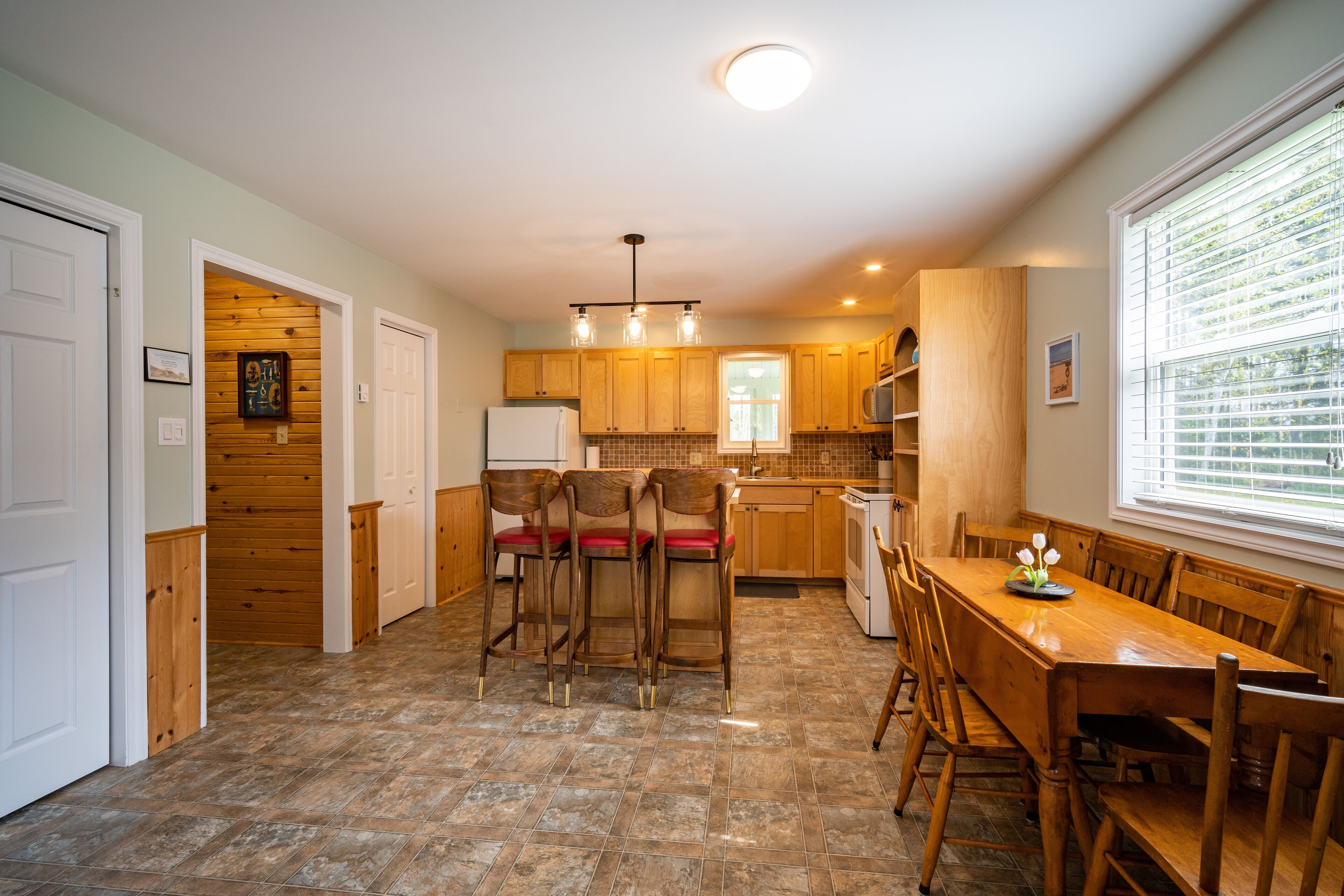 A kitchen with wooden cabinets, a dining table with chairs, and a window with blinds.