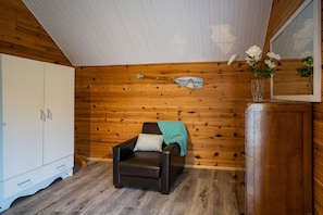 Una habitación con paneles de madera, un sillón de cuero marrón, un armario blanco y un jarrón con flores blancas.