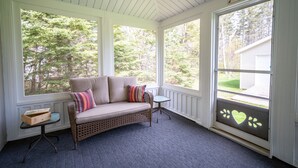A covered porch with a wicker sofa, a small table, and a window with a heart-shaped decoration. - Beach, Golf, Relax & Enjoy Our Beautiful Stanhope, PEI Cottage for your vacation (Stanhope)