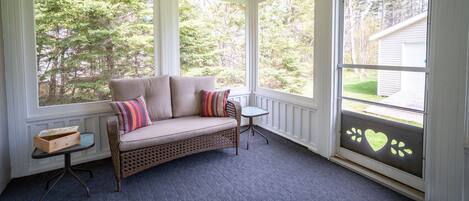 A covered porch with a wicker sofa, a small table, and a window with a heart-shaped decoration.