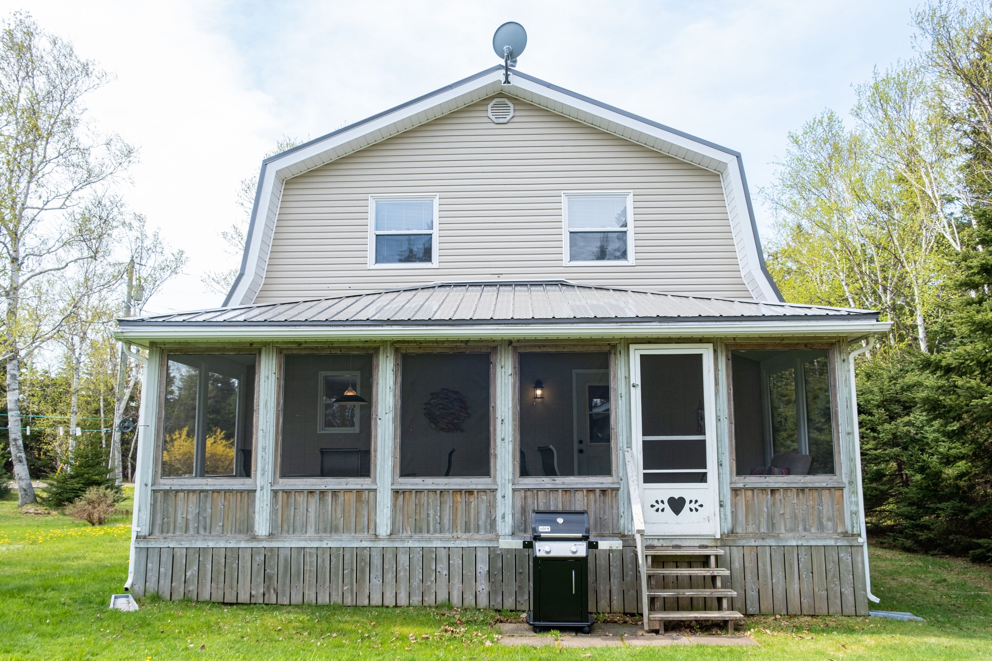 A two-story house with a covered porch, a satellite dish, and a grill outside.