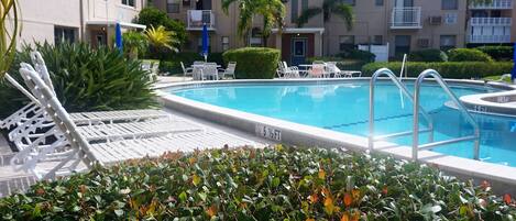 A swimming pool with lounge chairs and a hedge in the foreground.