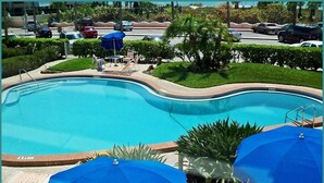 A swimming pool with lounge chairs and umbrellas, surrounded by greenery and a parking area. - Beach, Pool, Restaurants, Paradise ~ FN 803 (St Pete Beach)