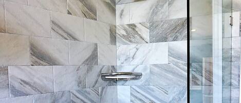 A shower with a glass door, marble tiles, and a handheld showerhead.