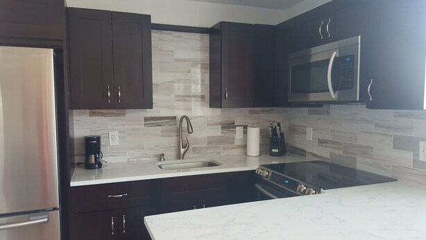A modern kitchen with dark cabinets, a stainless steel refrigerator, a microwave, a sink with a faucet, and a coffee maker. - Beach, Pool, Restaurants, Paradise ~ FN 803 (St Pete Beach)