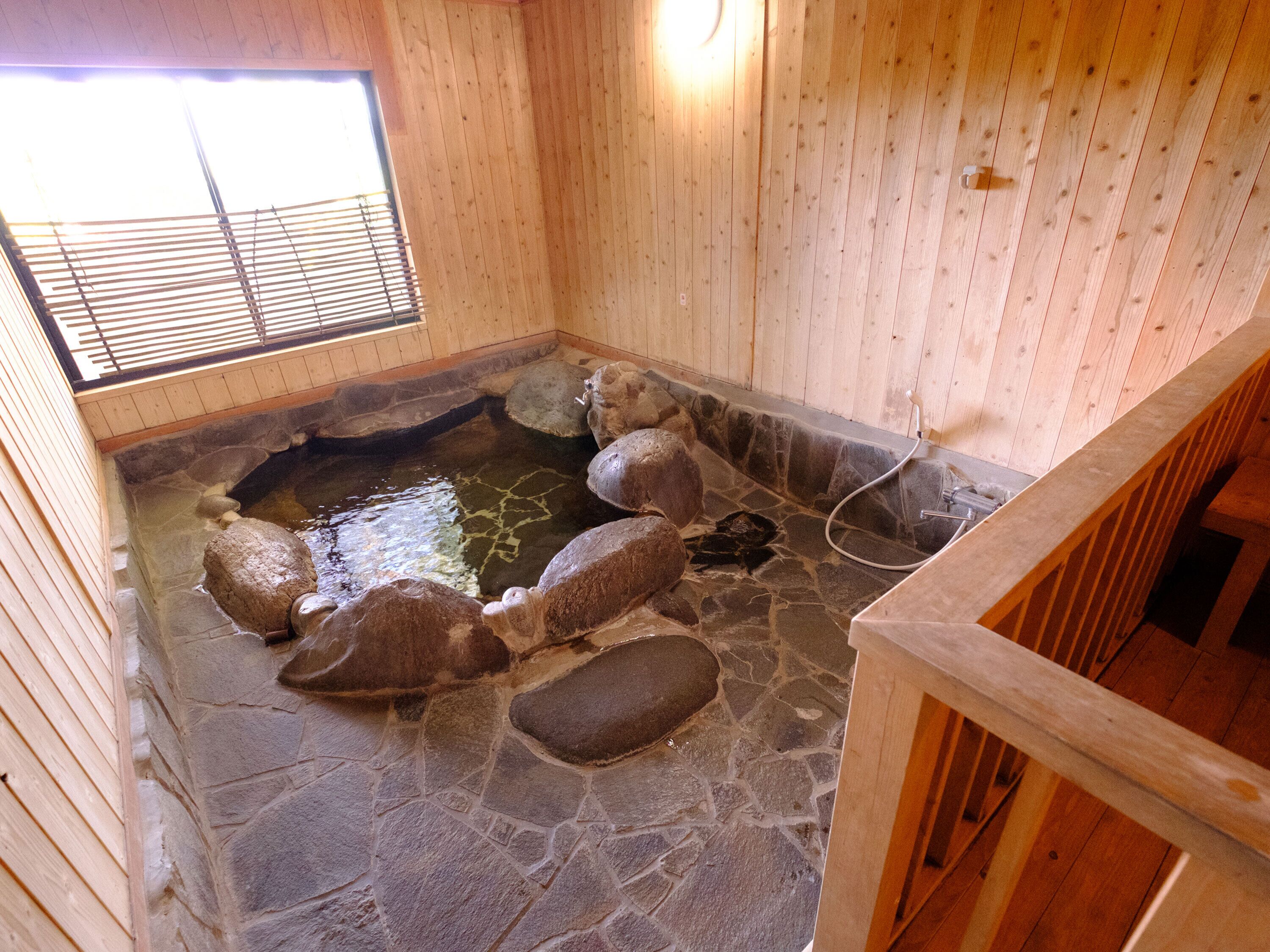 A stone hot spring bath with wooden walls and a wooden deck.