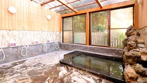 Uma área de spa com uma banheira de pedra quente, paredes de madeira e uma estrutura de vidro.